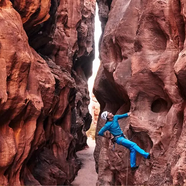 A rock climber scaling a red sandstone slot canyon